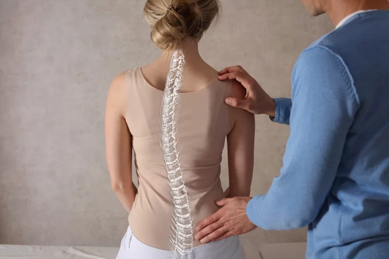 Žena s viditelným překrytím páteře sedí, zatímco muž zkoumá její záda a navrhuje chiropraktické sezení.